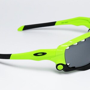 May include: Neon green and black sunglasses with gray lenses. The sunglasses have a sporty design with a wraparound frame. The arms are black at the tips and feature the brand's logo.