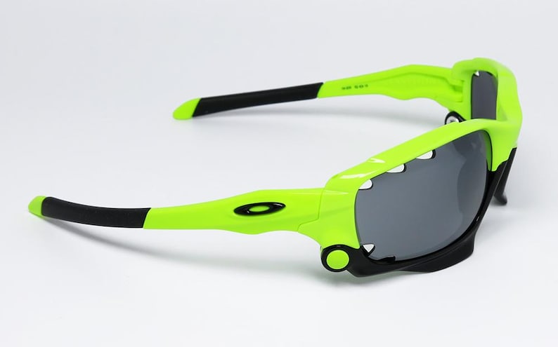 May include: Neon green and black sunglasses with gray lenses. The sunglasses have a sporty design with a wraparound frame. The arms are black at the tips and feature the brand's logo.