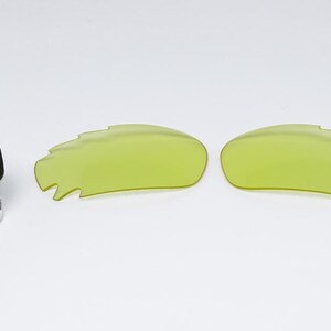 May include: A pair of neon yellow replacement lenses and a small bottle of cleaning solution. The lenses have a unique, jagged edge design. The cleaning solution bottle has a black cap and the text "NANO CLE" on the label.
