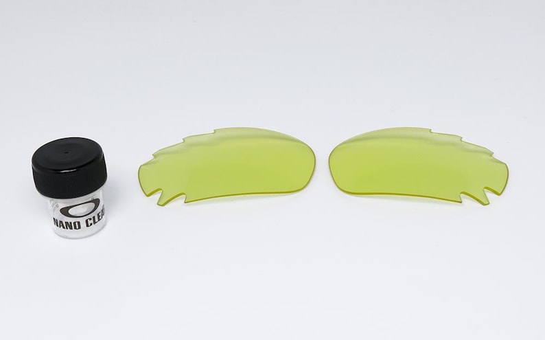 May include: A pair of neon yellow replacement lenses and a small bottle of cleaning solution. The lenses have a unique, jagged edge design. The cleaning solution bottle has a black cap and the text "NANO CLE" on the label.
