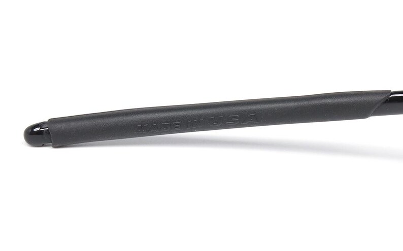 May include: Close-up of a black eyeglass arm with a rubberized grip. The text "MADE IN USA" is printed on the arm. The arm is black and has a curved shape.