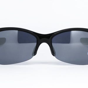 May include: Black sunglasses with gray lenses. The sunglasses have a semi-rimless design with a curved frame and a small logo sticker on the right lens. The lenses are a dark gray color, and the frame is glossy black.