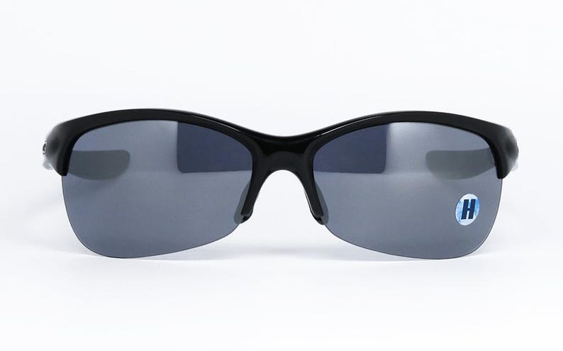 May include: Black sunglasses with gray lenses. The sunglasses have a semi-rimless design with a curved frame and a small logo sticker on the right lens. The lenses are a dark gray color, and the frame is glossy black.