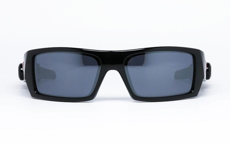 May include: Black sunglasses with a rectangular frame and gray lenses. The sunglasses have a thick, glossy frame and a modern, sporty design. The lenses are a dark gray color, providing protection from the sun.