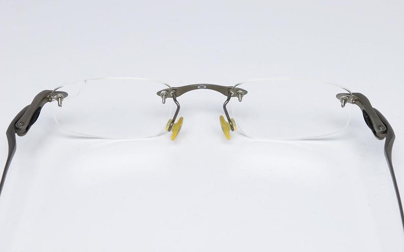 May include: A pair of rimless eyeglasses with a silver frame and clear lenses. The arms of the glasses are made of metal and have a silver finish.