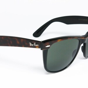 K&ouml;nnte beinhalten: Ray-Ban Wayfarer Sonnenbrille in Schildpatt-Optik mit gr&uuml;nen Gl&auml;sern. Die Sonnenbrille hat einen schwarzen Rahmen und ein silbernes Ray-Ban-Logo an der Seite.