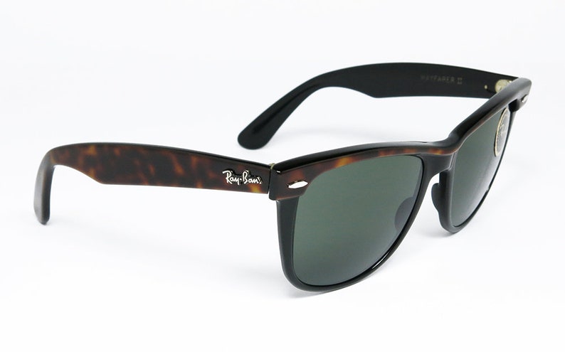 K&ouml;nnte beinhalten: Ray-Ban Wayfarer Sonnenbrille in Schildpatt-Optik mit gr&uuml;nen Gl&auml;sern. Die Sonnenbrille hat einen schwarzen Rahmen und ein silbernes Ray-Ban-Logo an der Seite.
