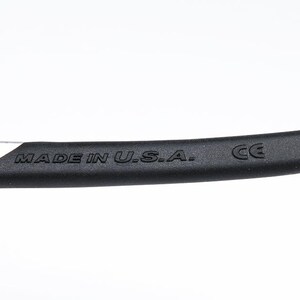 May include: Close-up of a silver and black arm of a pair of glasses with the text "MADE IN U.S.A." and "CE" printed on the arm.
