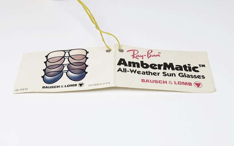 Puede incluir: Una etiqueta vintage de gafas de sol Ray-Ban AmberMatic All-Weather. La etiqueta presenta un gr&aacute;fico de gafas de sol en capas y el logotipo de Ray-Ban. Tambi&eacute;n se ve el texto "AmberMatic" y "Bausch & Lomb".