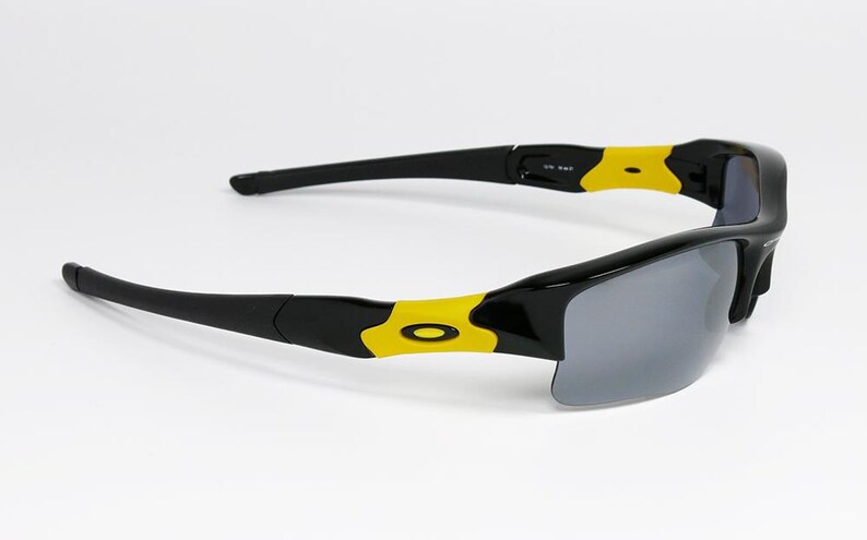 K&ouml;nnte beinhalten: Schwarze Sonnenbrille mit grauen Gl&auml;sern und gelben Akzenten. Die Sonnenbrille hat ein schlankes, modernes Design mit einem schwarzen Rahmen und gelben Details an den B&uuml;geln. Die Gl&auml;ser sind dunkelgrau.