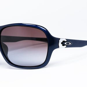 May include: Dark blue sunglasses with a gradient lens. The sunglasses have a thick frame and a silver accent on the temples. The lenses transition from brown to a lighter shade.