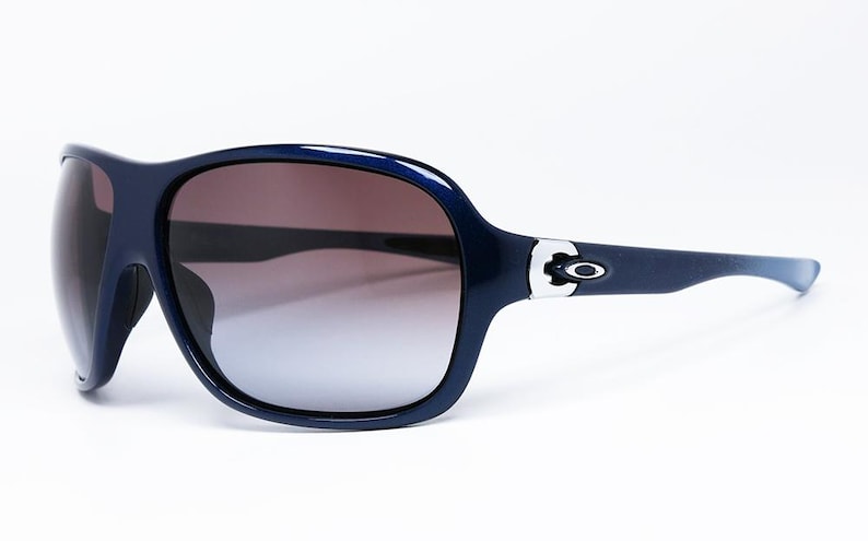 May include: Dark blue sunglasses with a gradient lens. The sunglasses have a thick frame and a silver accent on the temples. The lenses transition from brown to a lighter shade.