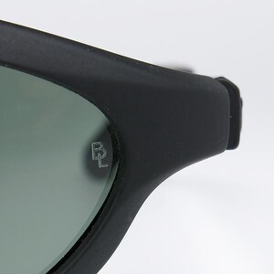 Pode incluir: Close-up de &oacute;culos de sol pretos com acabamento fosco. As lentes s&atilde;o de cor verde suave. O log&oacute;tipo da marca, um "BL" estilizado, est&aacute; gravado na lente. Os &oacute;culos de sol est&atilde;o sobre um fundo branco.