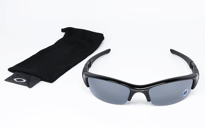 K&ouml;nnte beinhalten: Schwarze Sonnenbrille mit grauen Gl&auml;sern und einer schwarzen Tragetasche. Die Sonnenbrille hat ein schlankes, modernes Design mit einem geschwungenen Rahmen. Die Tasche ist ein weiches, schwarzes Etui.