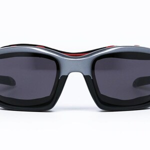 Puede incluir: Un par de gafas de sol negras y plateadas con detalles rojos. Las lentes son de color gris oscuro.