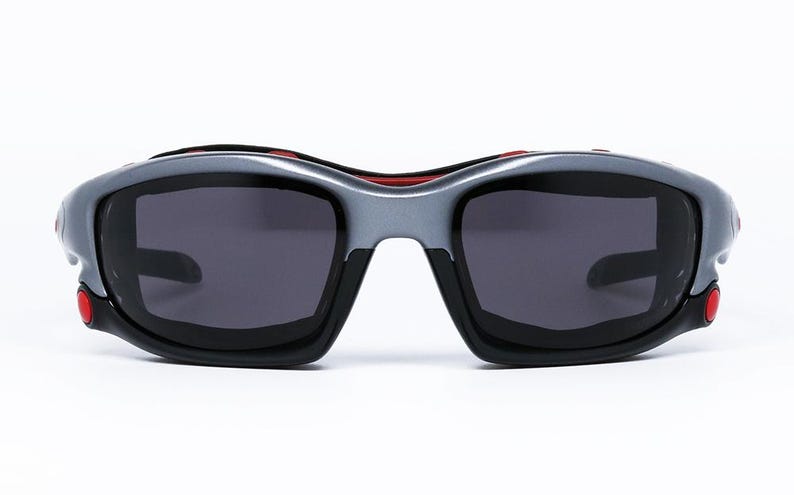 Puede incluir: Un par de gafas de sol negras y plateadas con detalles rojos. Las lentes son de color gris oscuro.