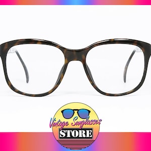 Può includere: Un paio di occhiali da vista in tartaruga con lenti trasparenti. Gli occhiali hanno una forma quadrata con bordi arrotondati.