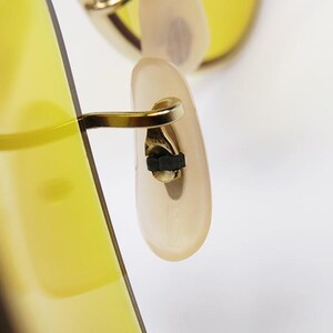 K&ouml;nnte beinhalten: Nahaufnahme des goldfarbenen Metall-Scharniers und des B&uuml;gelendes einer Sonnenbrille mit gelber T&ouml;nung.