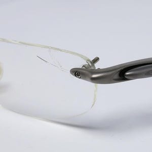 May include: A pair of silver-toned eyeglasses with clear frames and a broken lens. The glasses have a unique design with a hinge on the side.