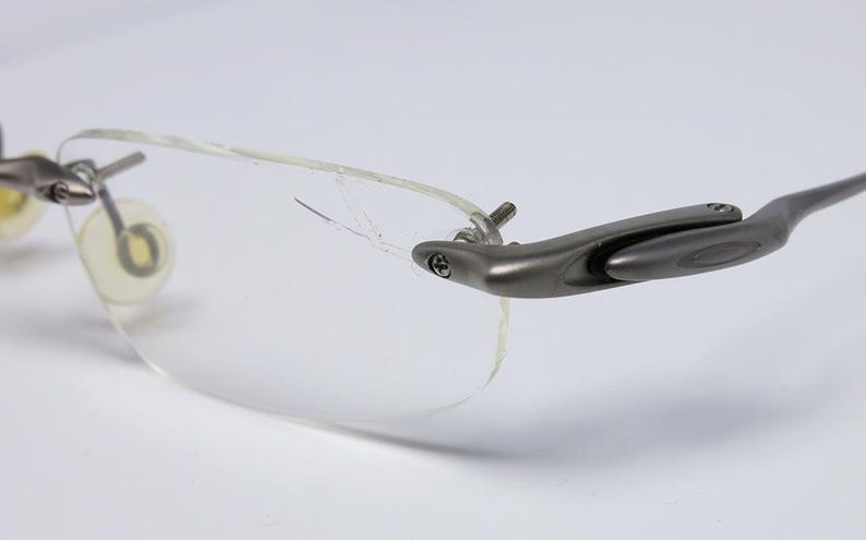 May include: A pair of silver-toned eyeglasses with clear frames and a broken lens. The glasses have a unique design with a hinge on the side.