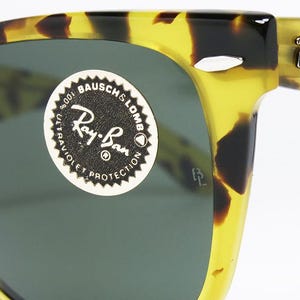 May include: Close-up of Ray-Ban sunglasses with a tortoise shell pattern. The sunglasses have dark lenses and the Ray-Ban logo is visible on the arm. A sticker on the lens reads "Ray-Ban" and "100% Ultraviolet Protection."
