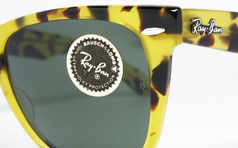 May include: Close-up of Ray-Ban sunglasses with a tortoise shell pattern. The sunglasses have dark lenses and the Ray-Ban logo is visible on the arm. A sticker on the lens reads "Ray-Ban" and "100% Ultraviolet Protection."
