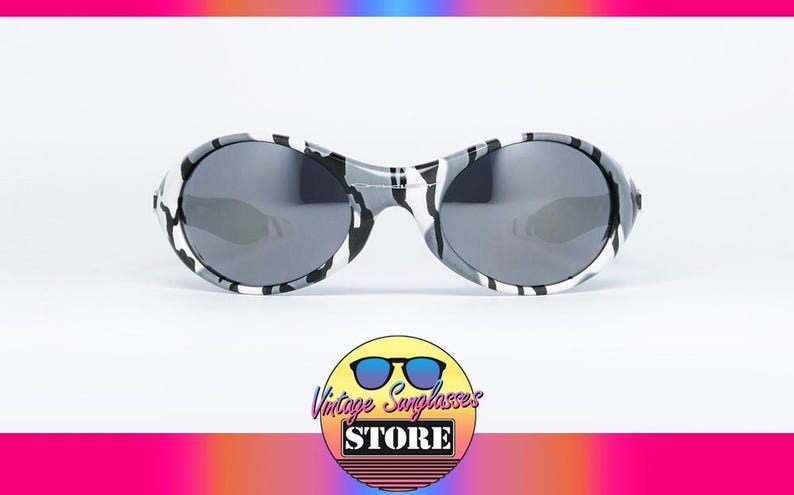 May include: Oval-shaped sunglasses with a black, white, and gray camouflage pattern on the frames. The lenses are a dark gray color. The sunglasses are displayed on a white background. The logo for Vintage Sunglasses Store is in the bottom center.