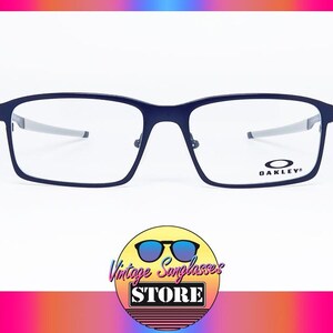 K&ouml;nnte beinhalten: Marineblaue Oakley-Brille mit rechteckigem Rahmen und silbernen B&uuml;geln. Das Oakley-Logo ist auf dem rechten Glas sichtbar. Das Bild enth&auml;lt ein Logo f&uuml;r Vintage Sunglasses Store.