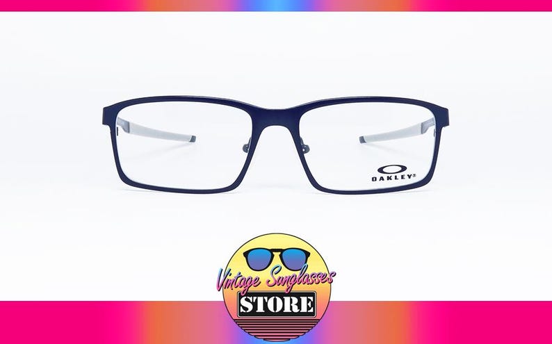 K&ouml;nnte beinhalten: Marineblaue Oakley-Brille mit rechteckigem Rahmen und silbernen B&uuml;geln. Das Oakley-Logo ist auf dem rechten Glas sichtbar. Das Bild enth&auml;lt ein Logo f&uuml;r Vintage Sunglasses Store.