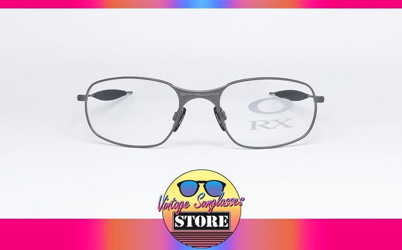 May include: Gray metal frame eyeglasses with clear lenses. The lenses have the text "RX" printed on them.