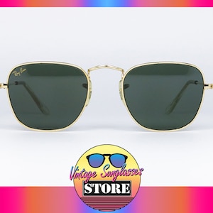 May include: Square sunglasses with gold frames and green lenses. The sunglasses have a Ray-Ban logo on the left lens.