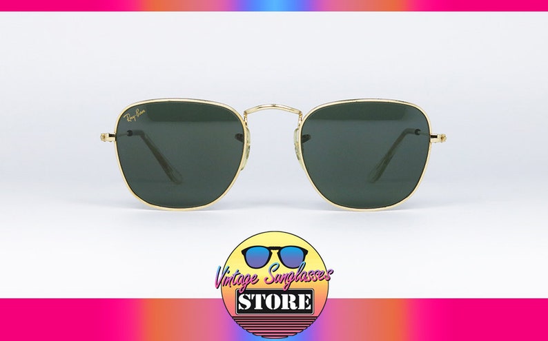 May include: Square sunglasses with gold frames and green lenses. The sunglasses have a Ray-Ban logo on the left lens.