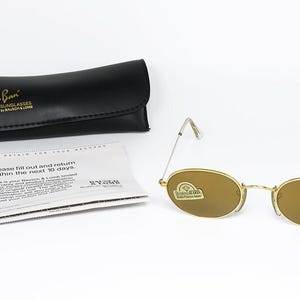 Pu&ograve; includere: Occhiali da sole Ray-Ban con montatura dorata e lenti ovali, una custodia in pelle nera e una scheda di garanzia. Gli occhiali da sole hanno un design classico, con una montatura in metallo dorato e lenti marroni. La custodia &egrave; nera con il logo Ray-Ban in oro.