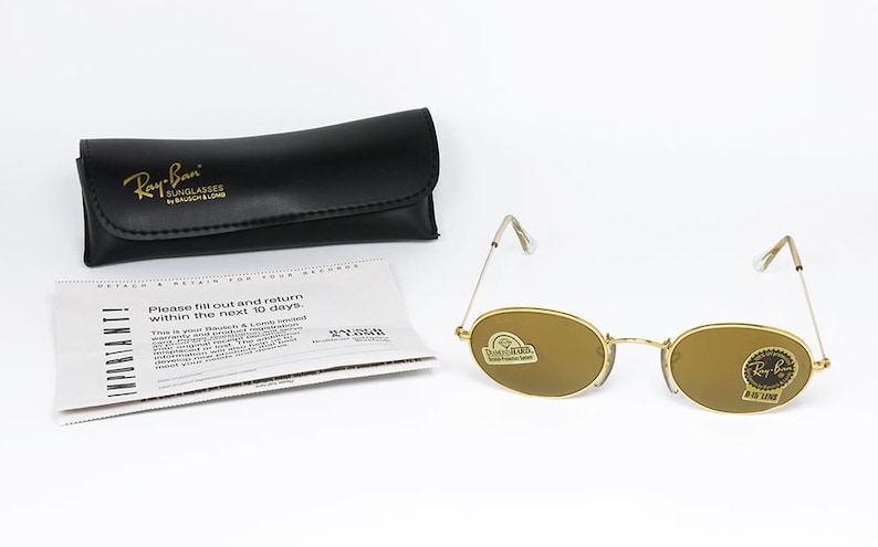 Pu&ograve; includere: Occhiali da sole Ray-Ban con montatura dorata e lenti ovali, una custodia in pelle nera e una scheda di garanzia. Gli occhiali da sole hanno un design classico, con una montatura in metallo dorato e lenti marroni. La custodia &egrave; nera con il logo Ray-Ban in oro.