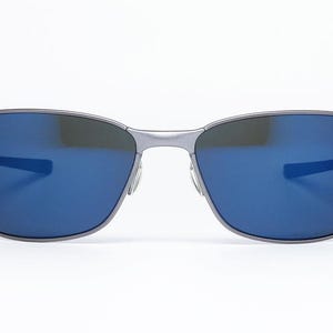 May include: A pair of sunglasses with a silver frame and blue lenses. The sunglasses have a rectangular shape with a bridge and temples. The lenses reflect light, and the overall design is sleek and modern.