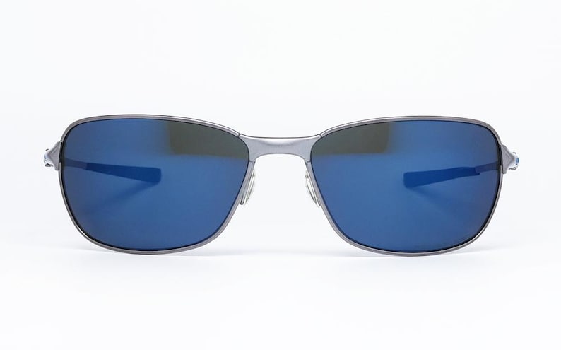 May include: A pair of sunglasses with a silver frame and blue lenses. The sunglasses have a rectangular shape with a bridge and temples. The lenses reflect light, and the overall design is sleek and modern.
