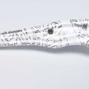 May include: White and black bicycle brake lever with a graphic design. The lever has a black grip and a black bolt. The text "004171-06 62" and "SAMPLE" is printed on the lever.
