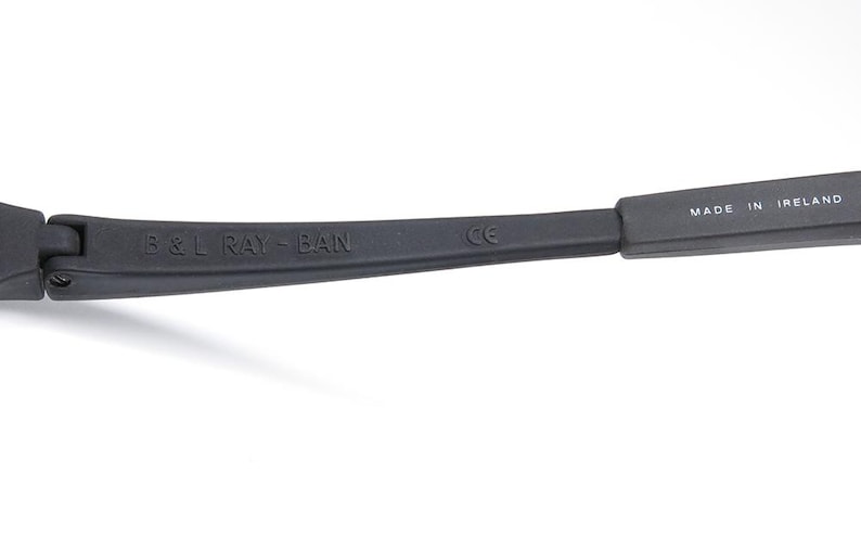 Pode incluir: Close-up de uma haste de &oacute;culos de sol Ray-Ban preta. O texto "B & L RAY-BAN" est&aacute; em relevo na haste. O texto "MADE IN IRELAND" tamb&eacute;m &eacute; vis&iacute;vel. A haste dos &oacute;culos de sol est&aacute; em um fundo branco.