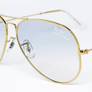 Op de afbeelding: Gouden aviator zonnebril met blauwe gradient lenzen. De zonnebril heeft een Ray-Ban logo op de rechter lens.