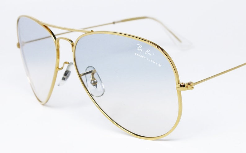 Op de afbeelding: Gouden aviator zonnebril met blauwe gradient lenzen. De zonnebril heeft een Ray-Ban logo op de rechter lens.