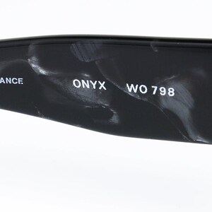 May include: Close-up of the inside of a black and white marbled sunglasses frame. The text "FRAME FRANCE ONYX WO 798" is printed on the frame.
