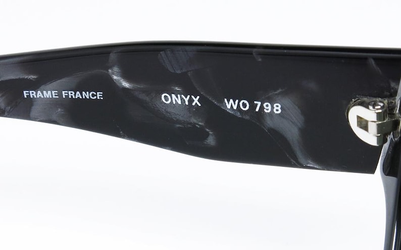 May include: Close-up of the inside of a black and white marbled sunglasses frame. The text "FRAME FRANCE ONYX WO 798" is printed on the frame.