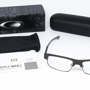 May include: An assortment of eyewear accessories, including a pair of rectangular eyeglasses with a black frame, a black carrying case, a black box, and a black drawstring pouch. A business reply mail envelope is also present.