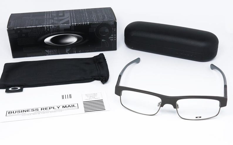 May include: An assortment of eyewear accessories, including a pair of rectangular eyeglasses with a black frame, a black carrying case, a black box, and a black drawstring pouch. A business reply mail envelope is also present.