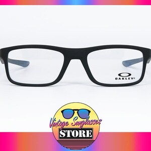 Puede incluir: Gafas Oakley negras con montura rectangular y lentes transparentes. El logotipo de Oakley es visible en la patilla derecha. La imagen también incluye un logotipo de Vintage Sunglasses Store.