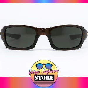 May include: Brown sunglasses with dark lenses. The rectangular frames have a slightly curved design. The image includes a logo for Vintage Sunglasses Store.