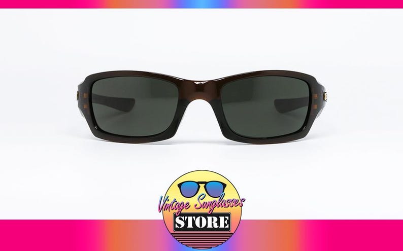 May include: Brown sunglasses with dark lenses. The rectangular frames have a slightly curved design. The image includes a logo for Vintage Sunglasses Store.