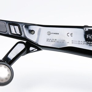 May include: Close-up of a black, glossy device with a circular light and text that reads "MADE IN SINGAPORE". The device has a sleek, modern design with metallic accents and a small, round light.