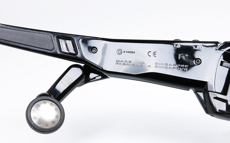 May include: Close-up of a black, glossy device with a circular light and text that reads "MADE IN SINGAPORE". The device has a sleek, modern design with metallic accents and a small, round light.