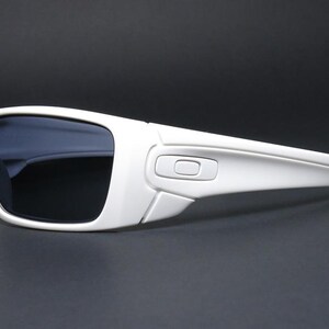 May include: White sunglasses with dark lenses. The sunglasses have a rectangular frame and a sleek, modern design. The arms of the sunglasses are thick and curve slightly. The lenses are dark, providing protection from the sun.